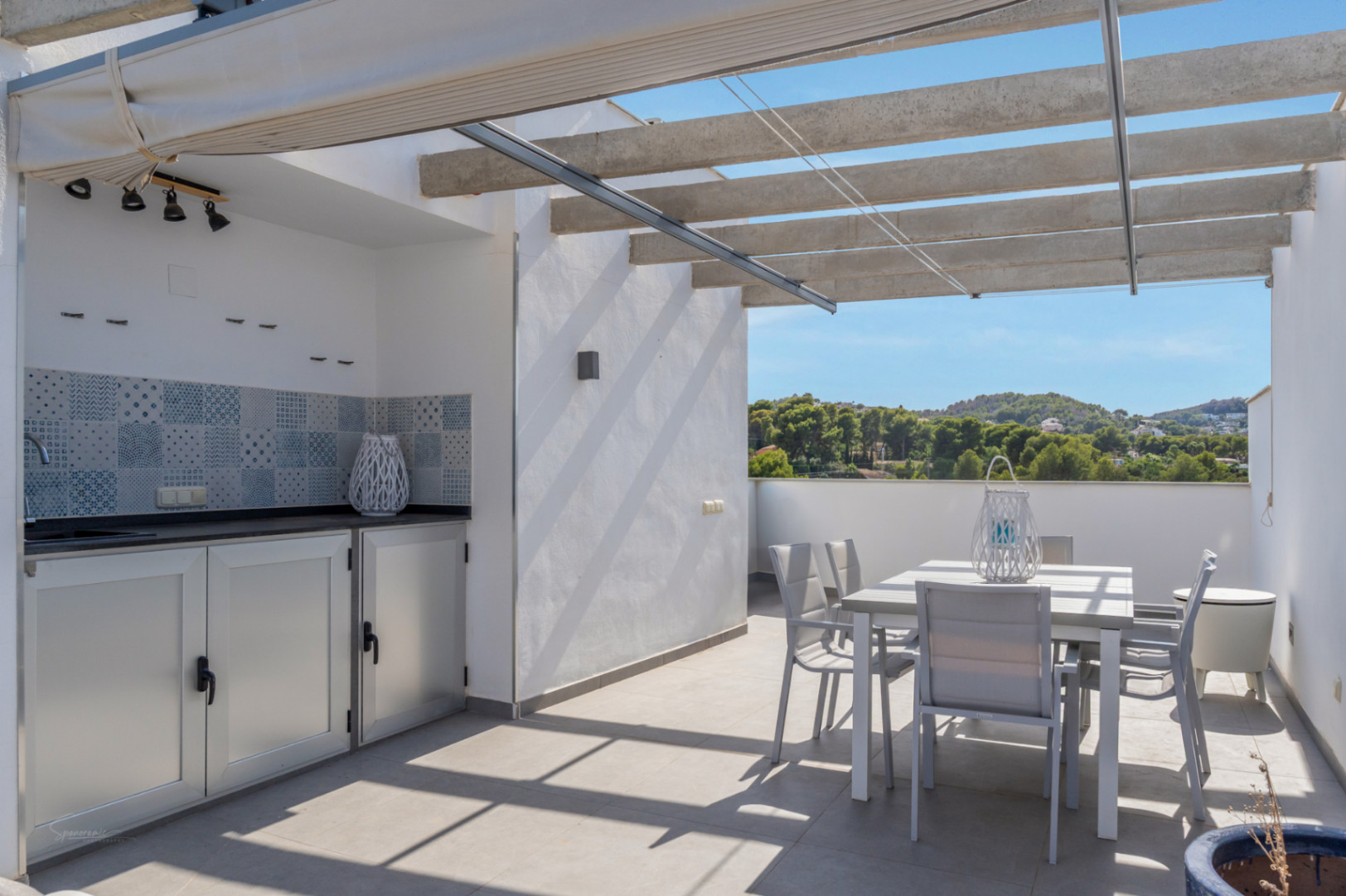 Privé dakterras met buitenkeuken, eethoek en een betonnen pergola met zonnescherm, uitkijkend over de groene heuvels en de natuurlijke omgeving.