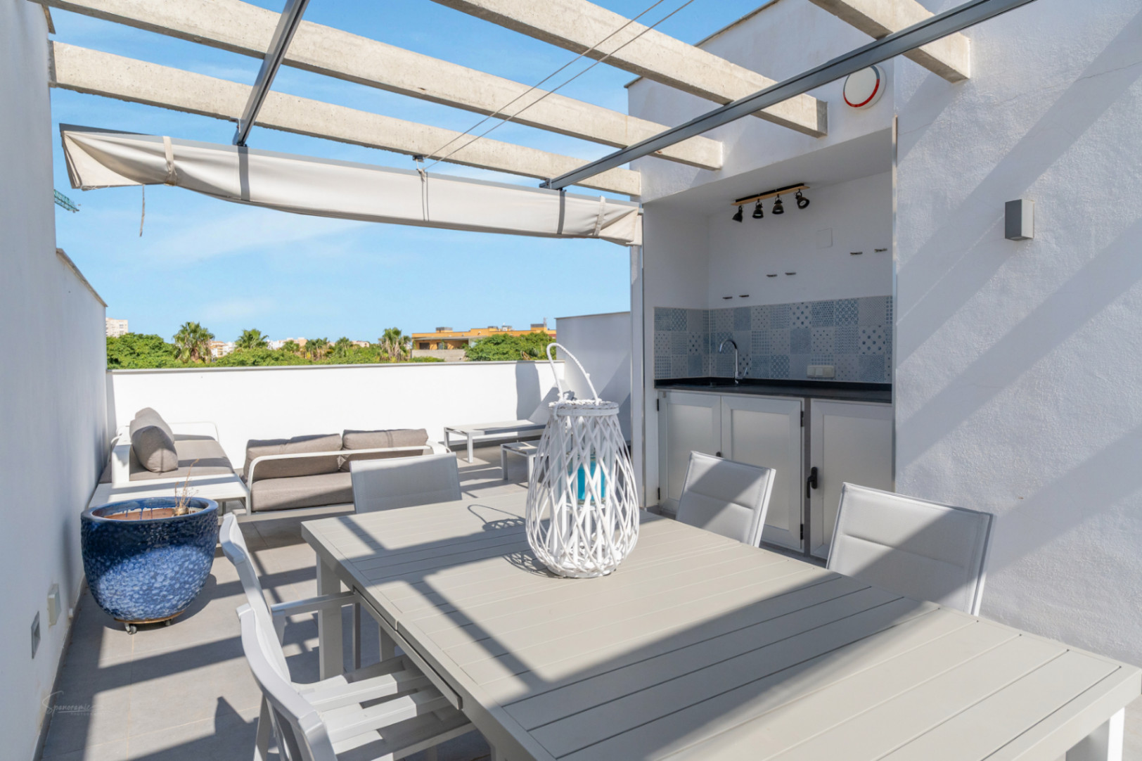 Privé dakterras met buitenkeuken, eethoek en loungegedeelte onder een betonnen pergola met uitschuifbaar zonnescherm en vrij uitzicht.