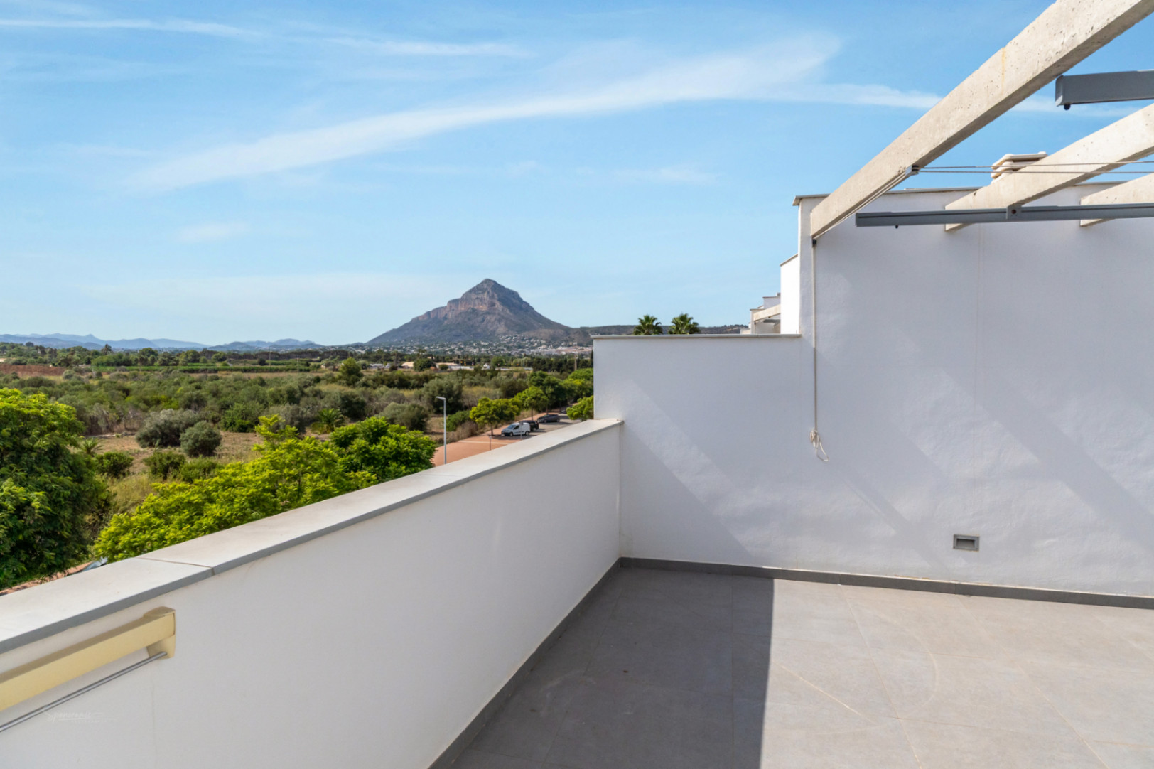 Privé dakterras met grijze tegels en een betonnen pergola, met panoramisch uitzicht op de berg Montgó en de omliggende groene velden.