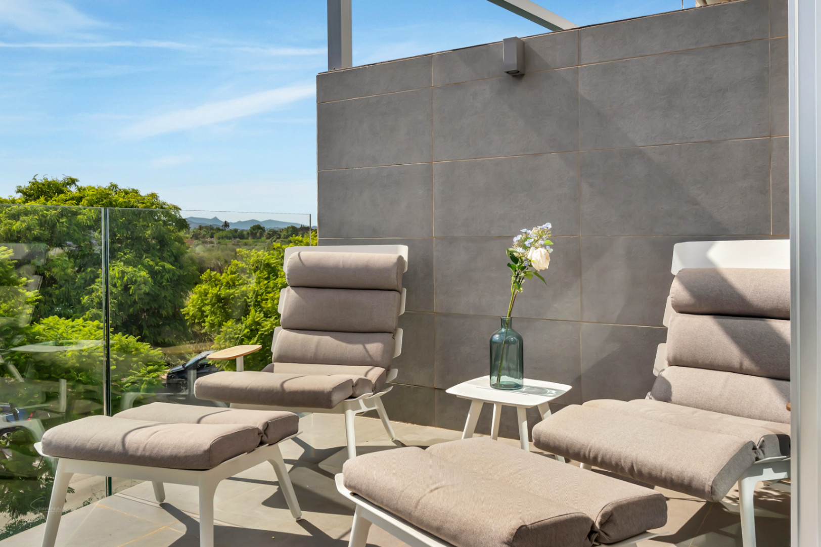 Privéterras met modern loungemeubilair, glazen balustrade en vrij uitzicht over de natuurlijke velden en bergen.