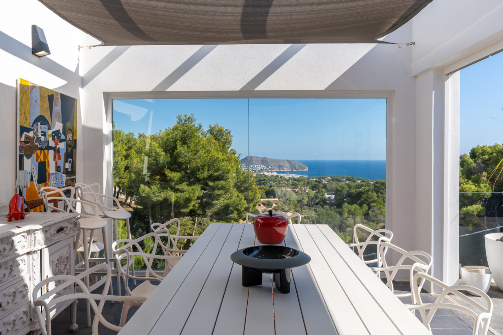 Buiten-eethoek met witte tafel en designstoelen onder een schaduwdoek, met panoramisch uitzicht op de Middellandse Zee en de kustlijn van Moraira.