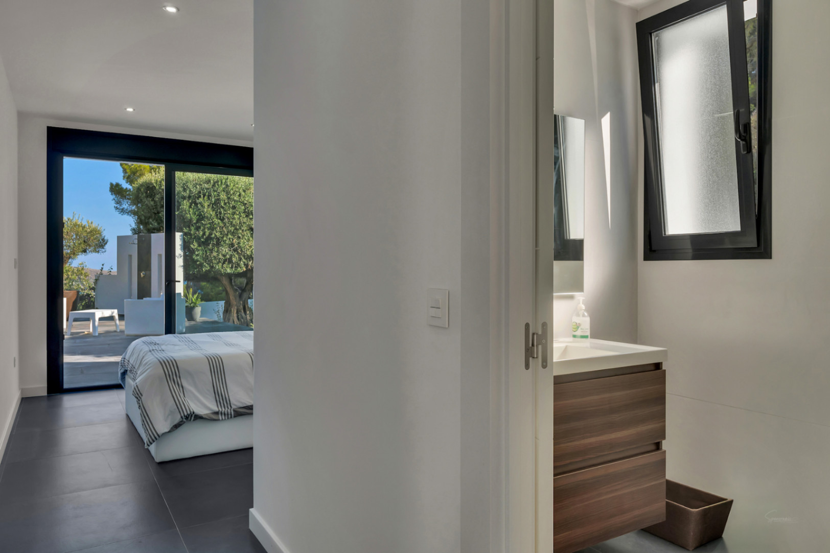 En-suite slaapkamer met donkere vloertegels, directe toegang tot het terras en een moderne badkamer met houten wastafelmeubel.