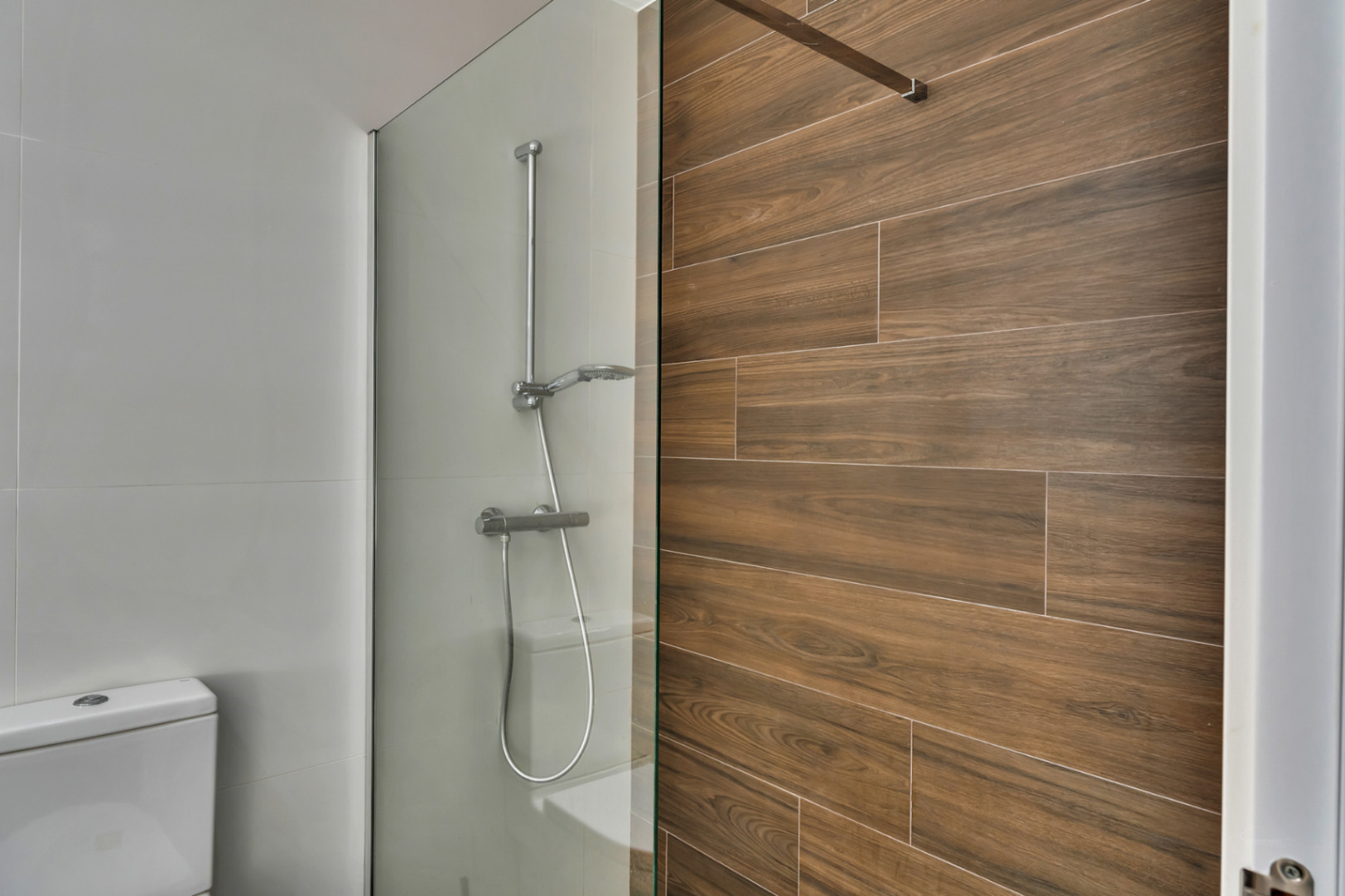 Moderne badkamer met inloopdouche, glazen wand en een accentmuur van keramische tegels met houtlook.