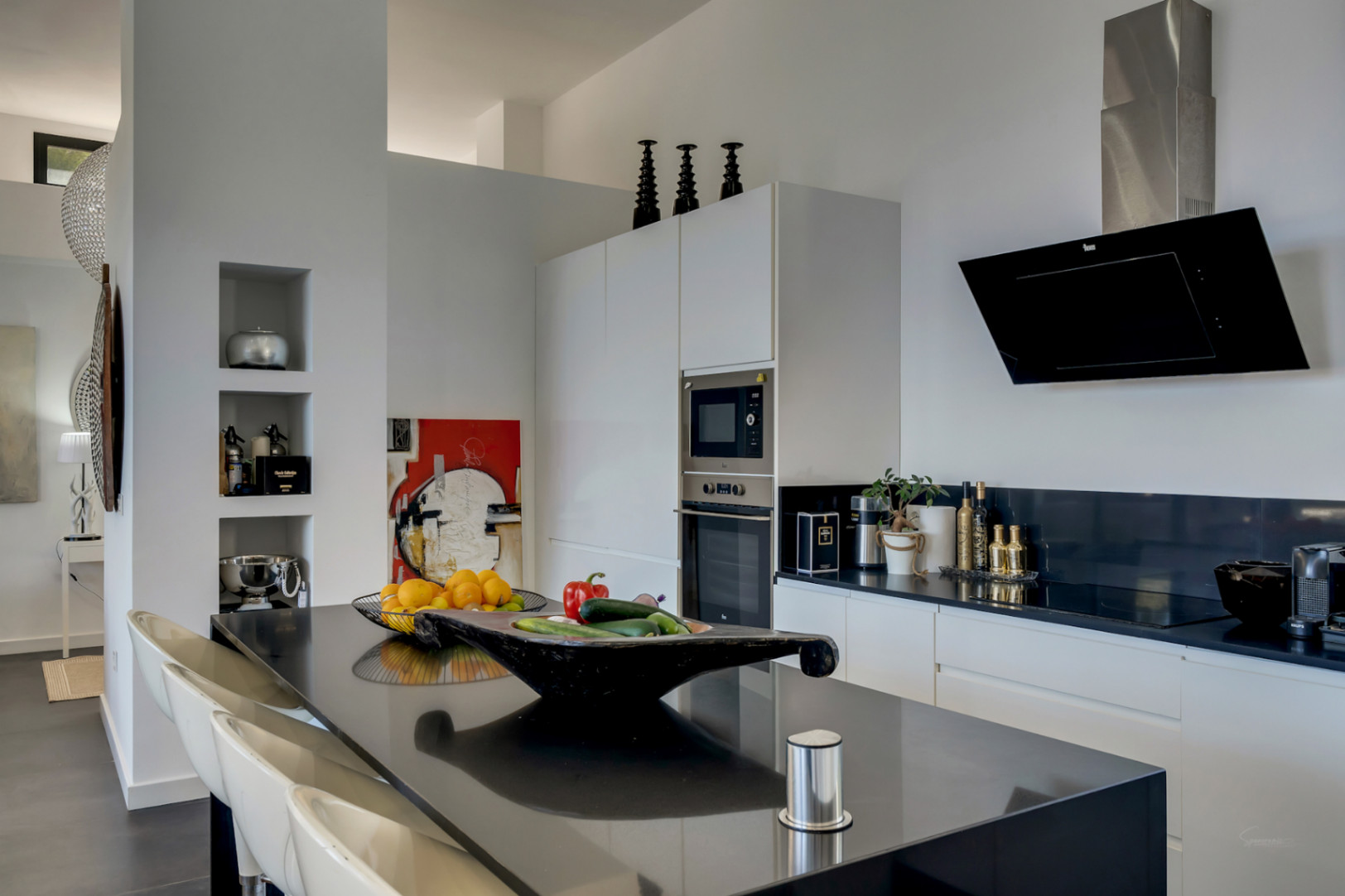 Moderne keuken met een strak zwart kookeiland, geïntegreerde apparatuur en witte kasten. Voorzien van een design afzuigkap en ingebouwde nissen in de wand.