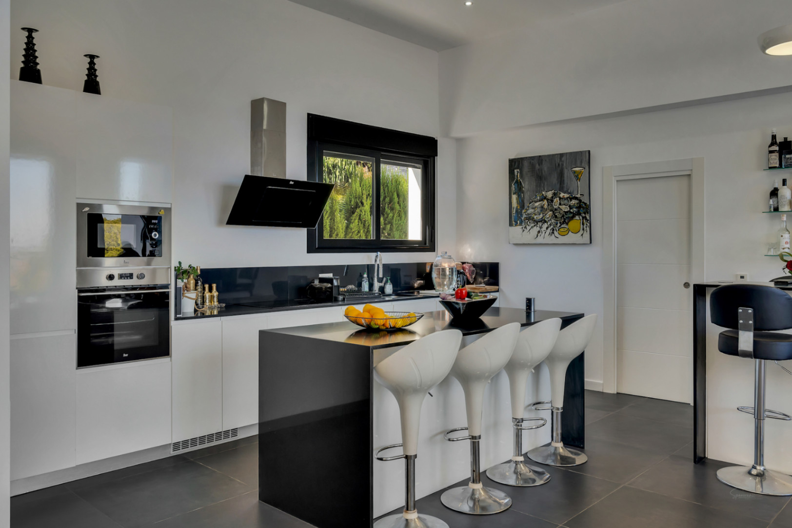 Moderne keuken met zwart kookeiland, witte barkrukken, geïntegreerde apparatuur en een strak zwart-wit interieurontwerp.