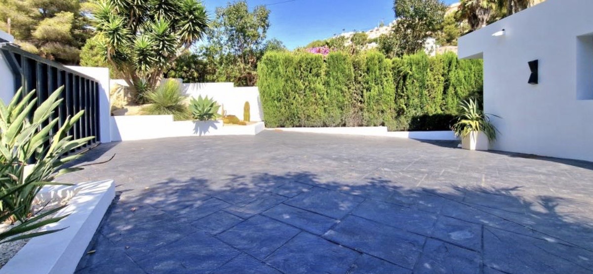 Ruime oprit met donkergrijs motiefbeton, omzoomd door witte muren en een mediterrane tuin met yucca's en een dichte cipressenhaag.