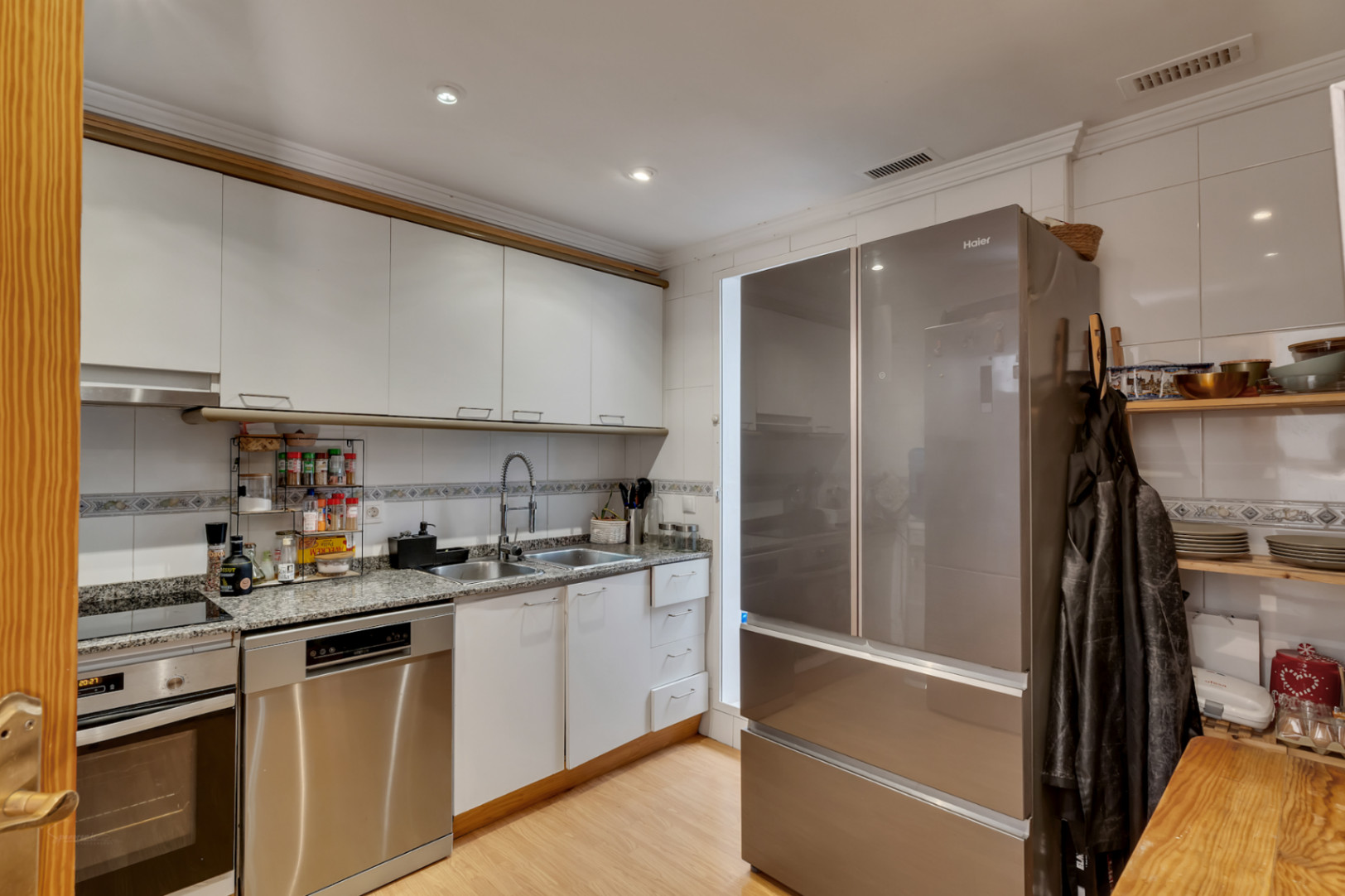 Functionele keuken met witte kasten, granieten werkblad en roestvrijstalen apparatuur, inclusief een grote koel-vriescombinatie en geïntegreerde vaatwasser.