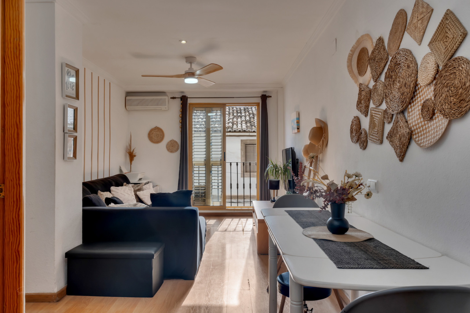 Lichte woon- en eetkamer met houten vloer, plafondventilator en schuifpui naar een balkon met uitzicht op de karakteristieke daken van de oude stad.