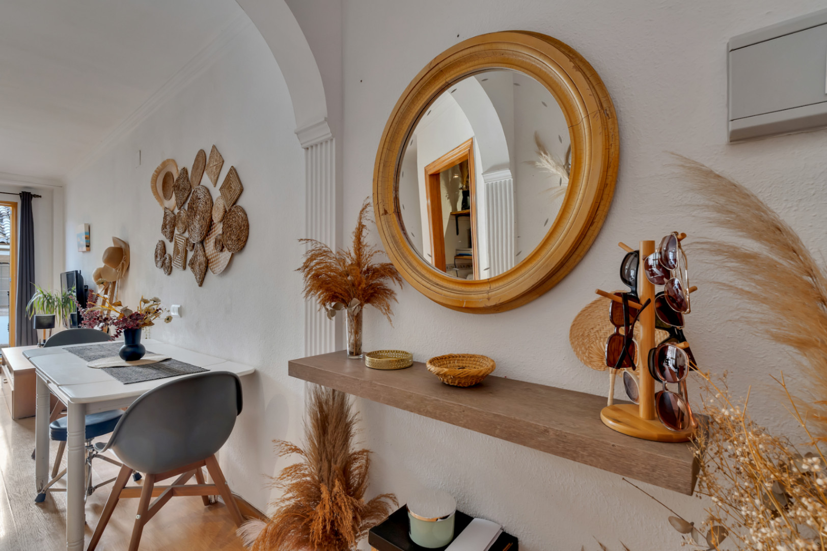 Sfeervolle entree met een ronde houten spiegel, zwevende plank en natuurlijke decoraties, grenzend aan de lichte open eetkamer.