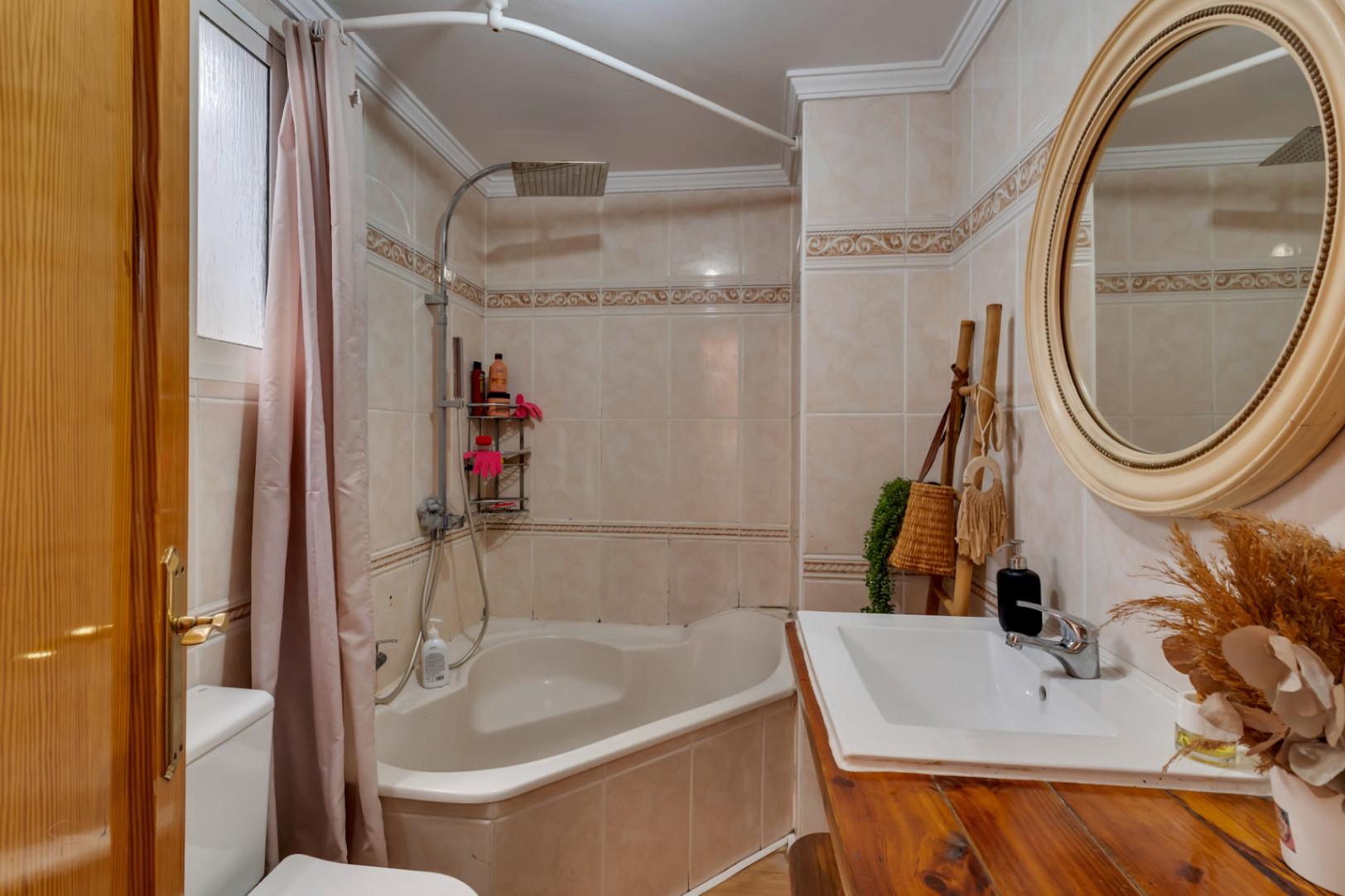 Volledige badkamer met hoekbad, regendouche en een rustiek houten wastafelmeubel. Voorzien van een ronde spiegel en wandtegels met een klassieke bies.