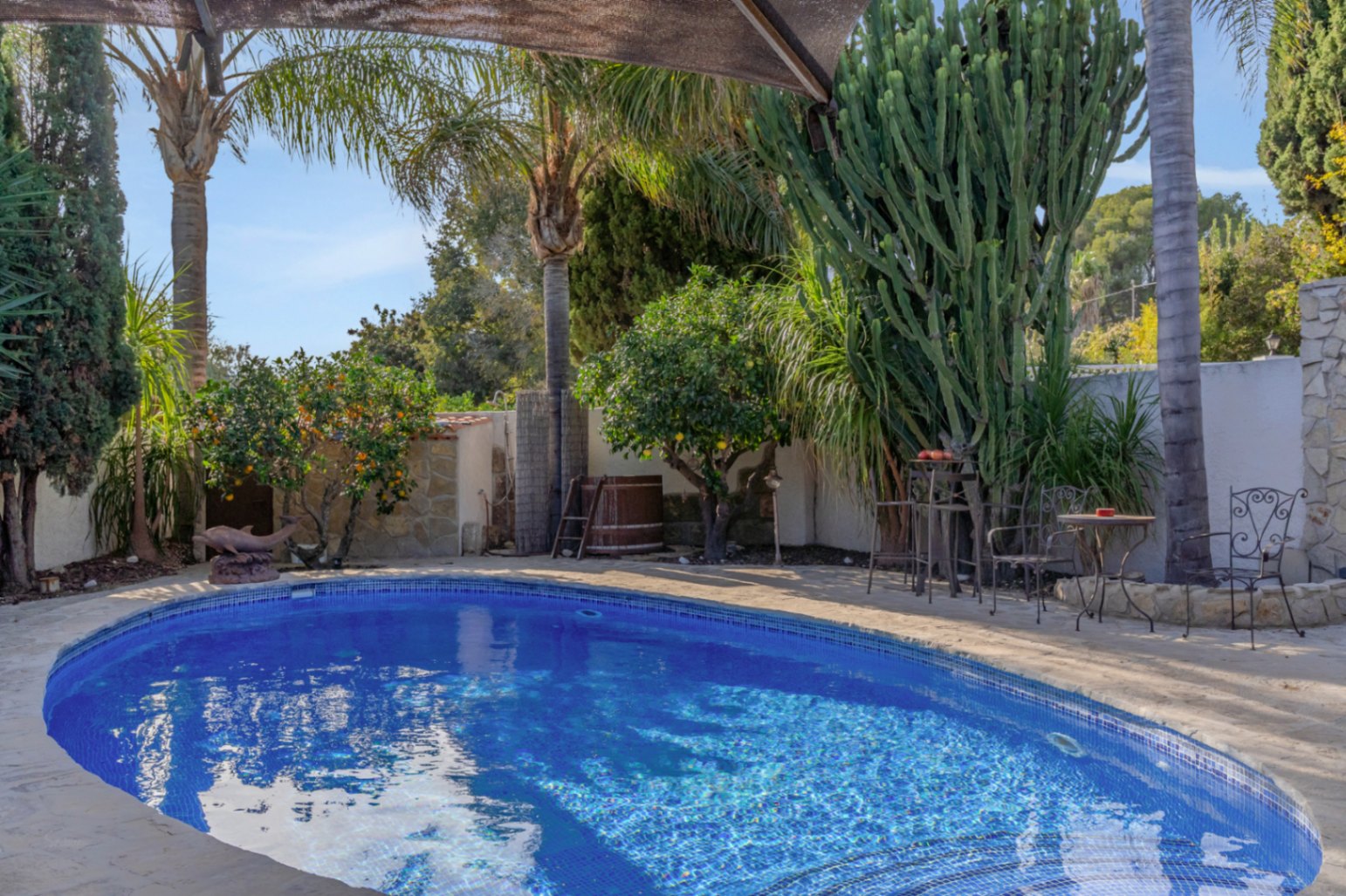 Privézwembad met blauwe mozaïektegels, omgeven door een mediterrane tuin met palmbomen, citrusbomen en een smeedijzeren zithoek op een natuurstenen terras.