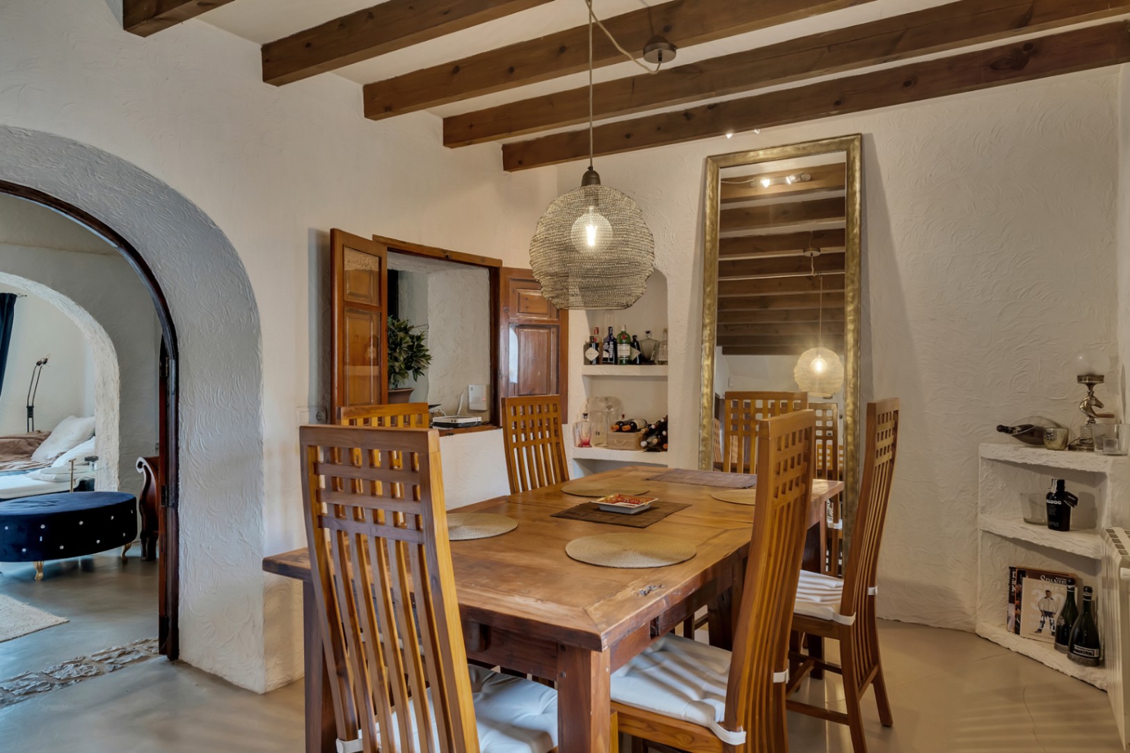 Rustieke eethoek met houten balkenplafond, een massief houten tafel en stoelen met hoge rugleuning. Voorzien van een doorgeefluik met houten luiken en een karakteristieke boogdoorgang.