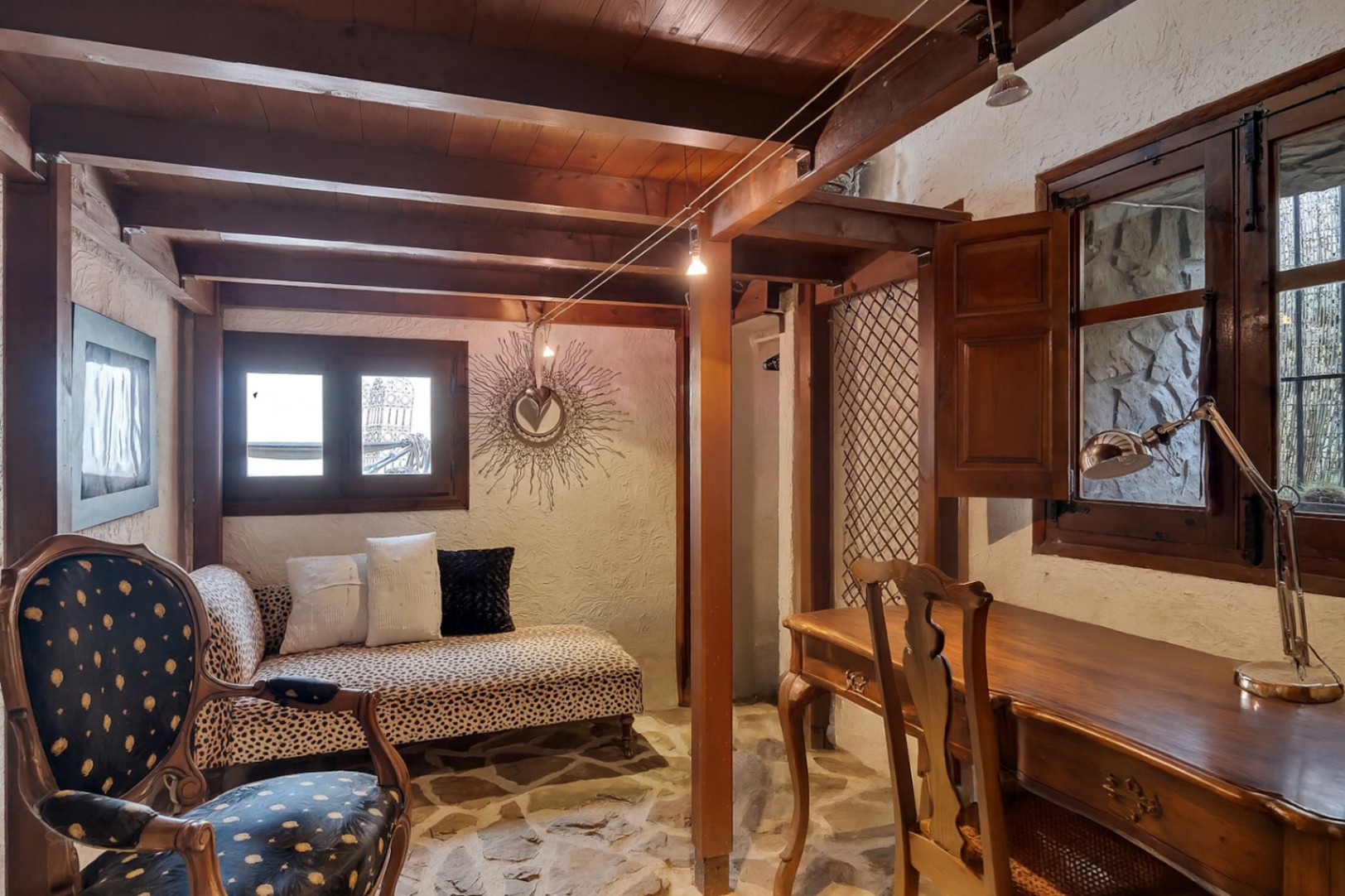 Rustieke werkkamer met houten balkenplafond, natuurstenen vloer, klassiek houten bureau en een chaise longue met dierenprint.