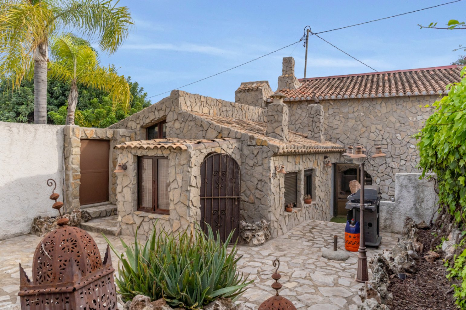 Vrijstaand gastenverblijf met natuurstenen gevels, terracotta dakpannen en een geplaveid terras voorzien van een barbecue en mediterrane beplanting.