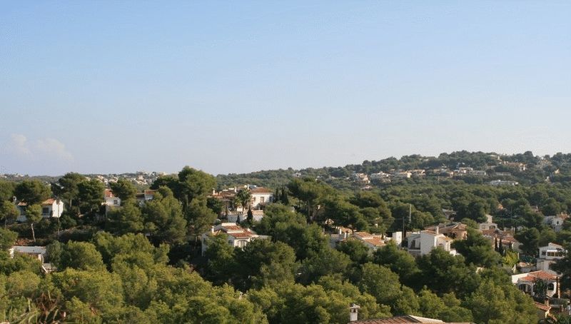 Panoramisch uitzicht vanaf het perceel over een residentiële vallei met traditionele witte villa's en dichte mediterrane dennenbossen.