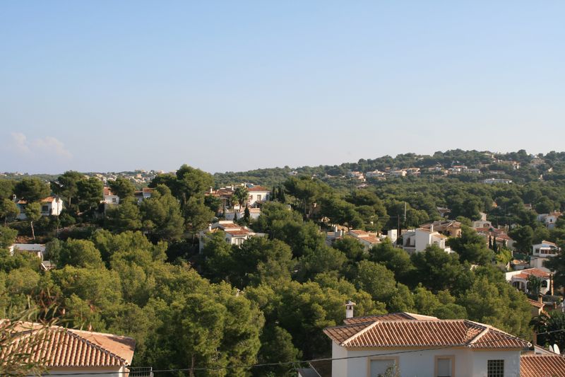 Panoramisch uitzicht vanaf het perceel over een woonwijk in een mediterraan dennenbos, met traditionele villa's en karakteristieke pannendaken.