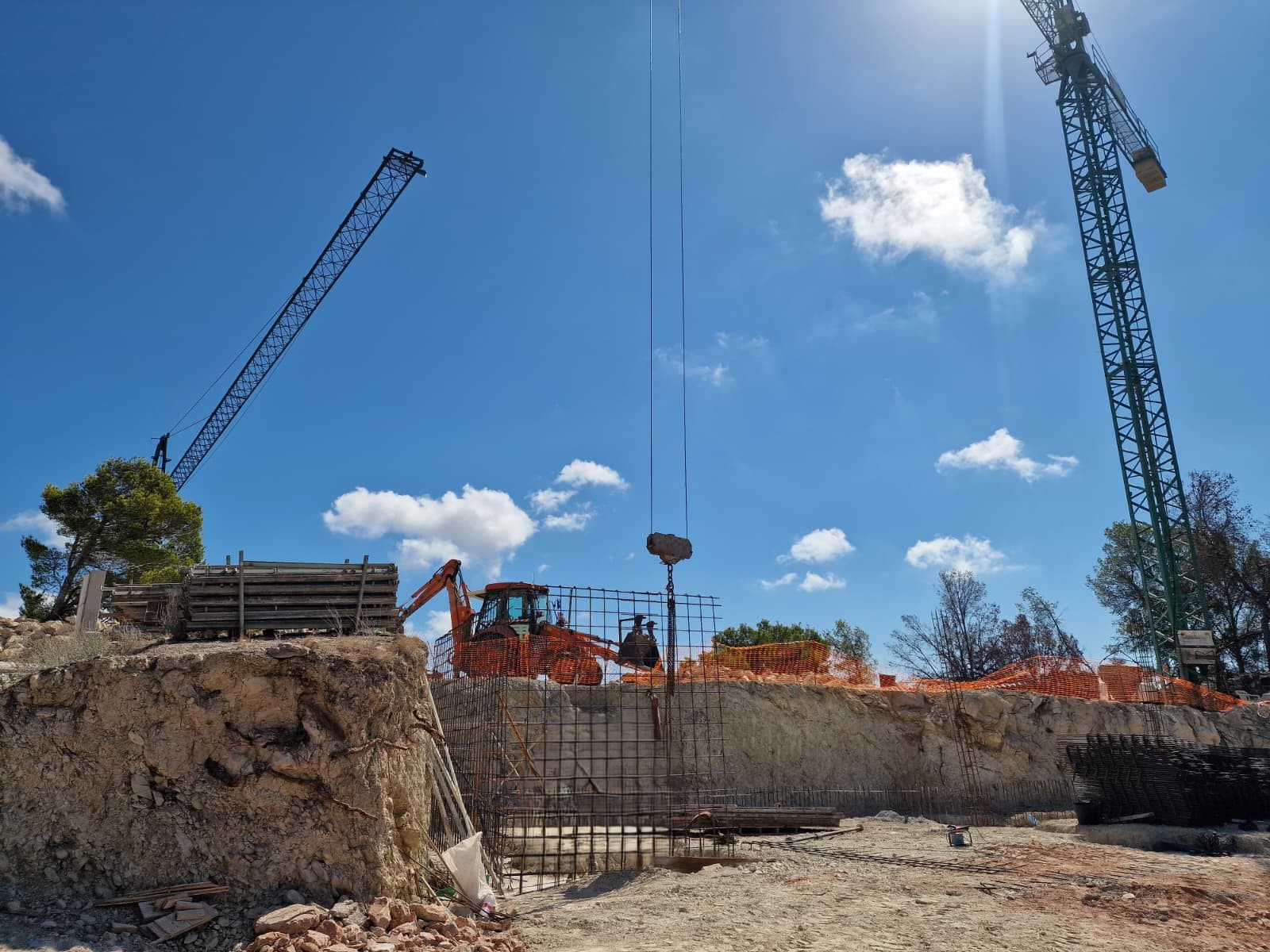 Voortgang van de bouw in Moraira met grondverzet, staalvlechtwerk voor de fundering en de aanwezigheid van bouwkranen op het perceel.