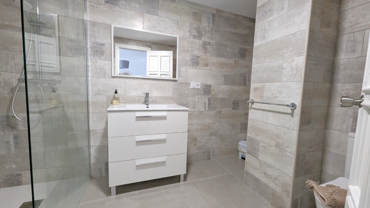 Moderne badkamer met een wit badkamermeubel met drie laden, een inloopdouche met glazen wand en wandtegels met textuur in neutrale tinten.