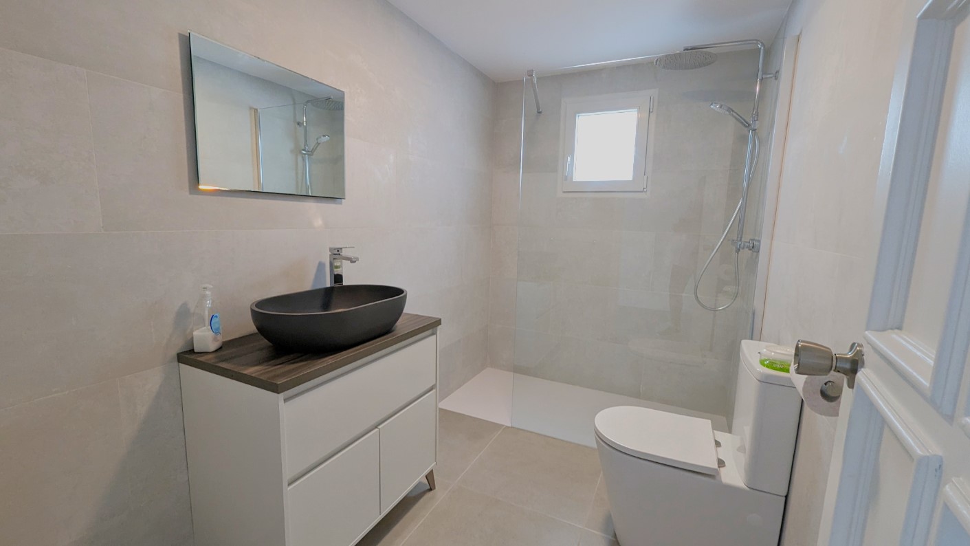 Moderne badkamer met een zwarte opzetwastafel, inloopdouche met glazen wand en grote grijze tegels voor een strakke, eigentijdse afwerking.