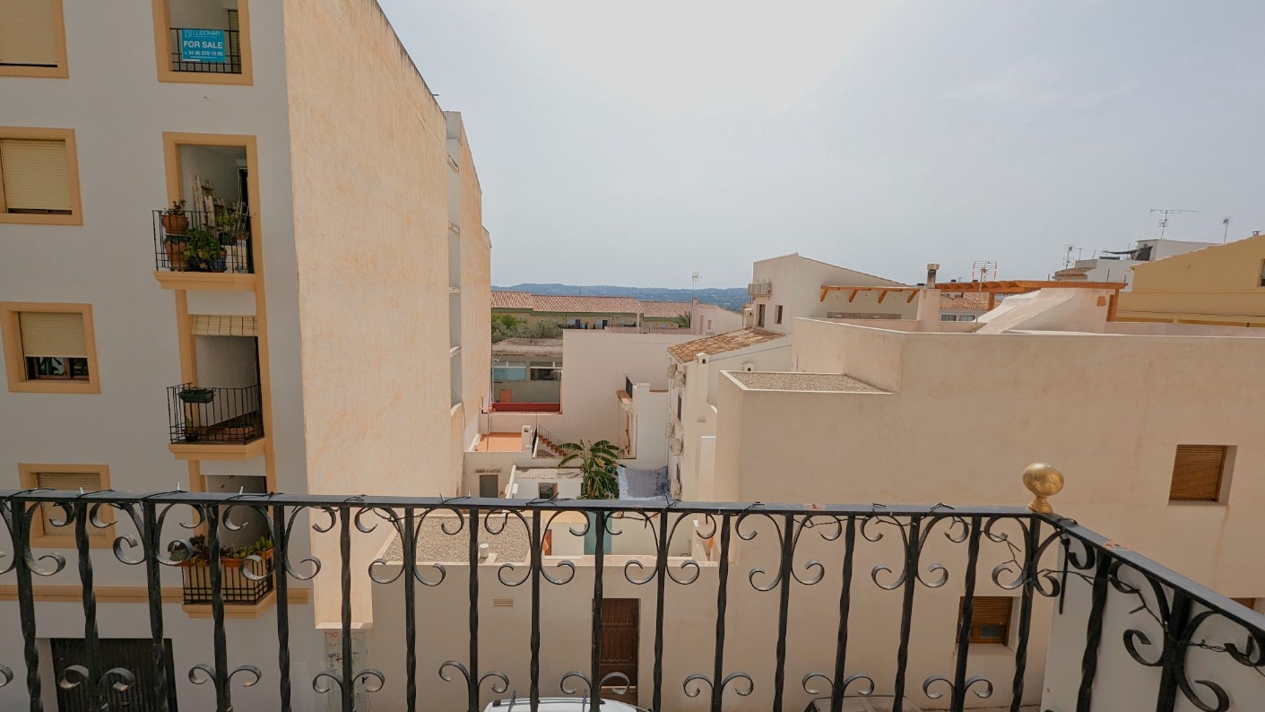 Uitzicht vanaf het balkon met smeedijzeren balustrade over de daken van de oude stad van Javea richting de verre bergachtige horizon.