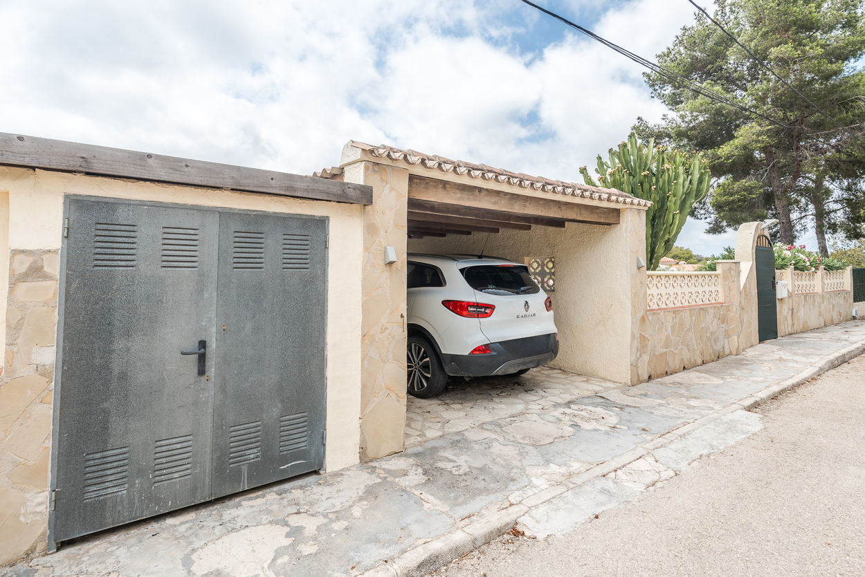Exterieur met omheinde entree, natuurstenen muren en een overdekte carport met houten balken voor veilig parkeren op eigen terrein.