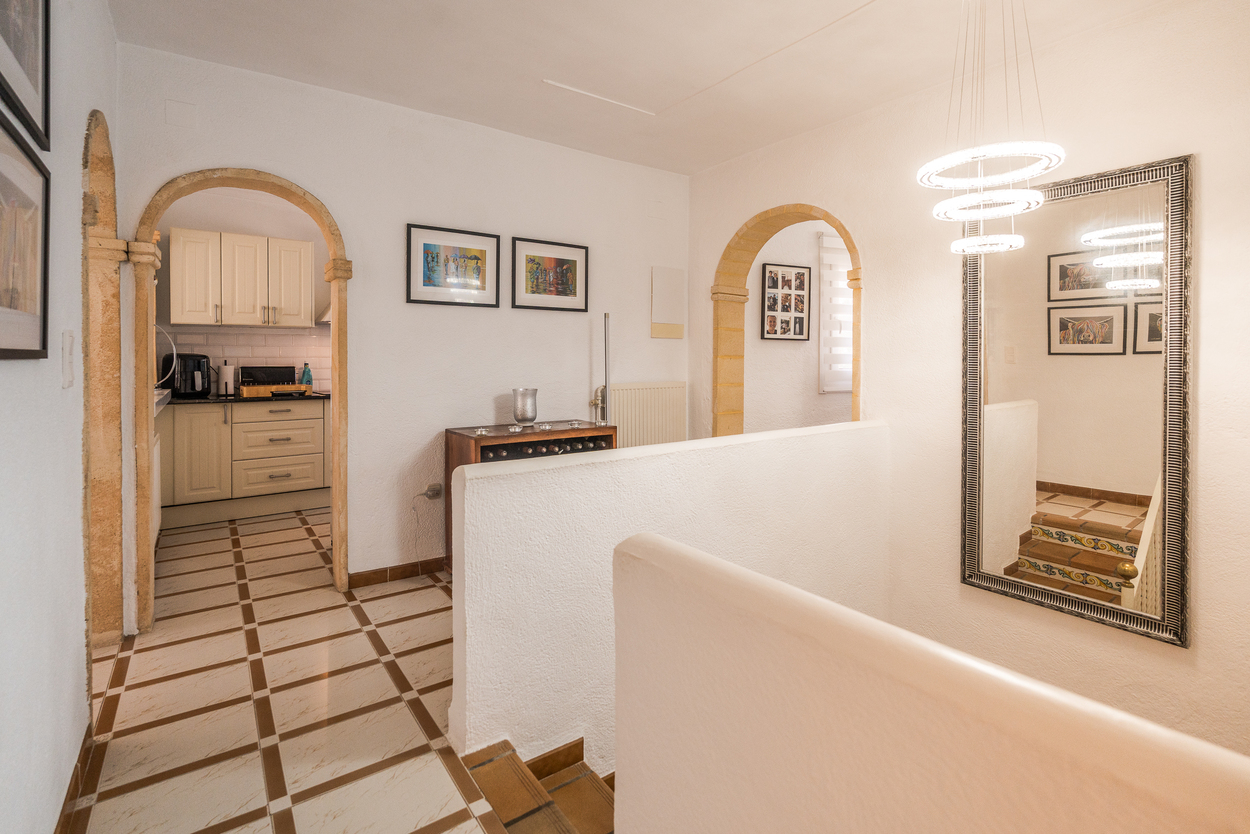 Hal met Tosca stenen bogen, tegelvloer en een moderne ronde kroonluchter. Biedt toegang tot de keuken en een trap met decoratieve tegels op de stootborden.