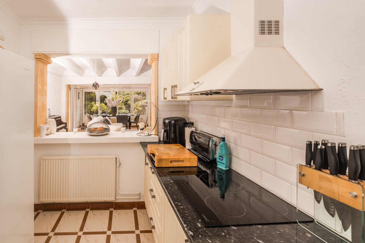 Ingerichte keuken met donkere granieten werkbladen, metrotegels en een ontbijtbar die via tosca stenen pilaren uitkijkt op de woonkamer.