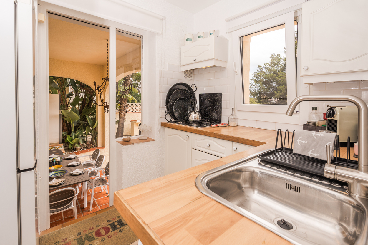 Ingerichte keuken met houten werkbladen, metrotegels en directe toegang tot een overdekte naya met eethoek onder mediterrane bogen.