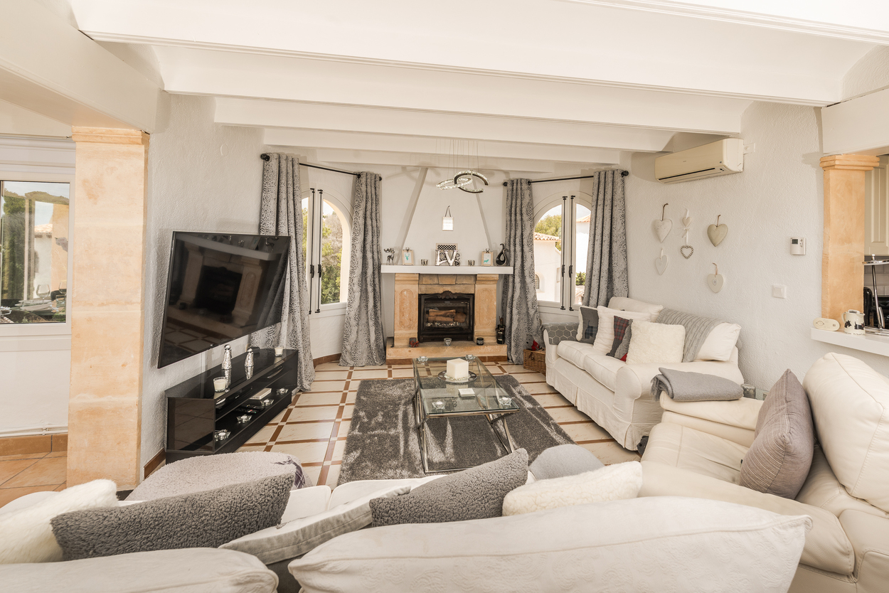 Lichte woonkamer met een natuurstenen Tosca openhaard, wit balkenplafond, stenen pilaren en traditionele tegelvloer.