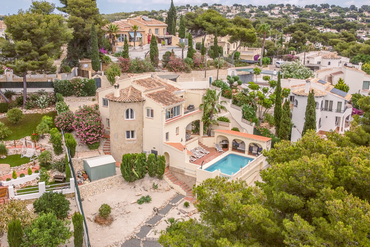 Luchtfoto van de op het zuiden gelegen villa met natuurstenen toren, terrassen op verschillende niveaus en een 8x4m zwembad met overdekte barbecueplaats.
