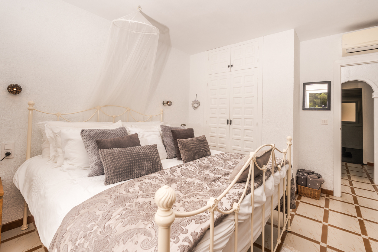 Slaapkamer met wit smeedijzeren bed, klamboe en ingebouwde kasten. Voorzien van een tegelvloer en airconditioning boven de gewelfde doorgang.