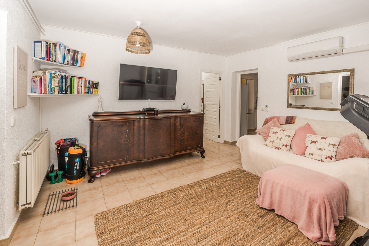 Woonkamer met een groot houten dressoir, wandtelevisie en tegelvloer. Voorzien van centrale verwarming, airconditioning en een natuurlijk vezeltapijt.