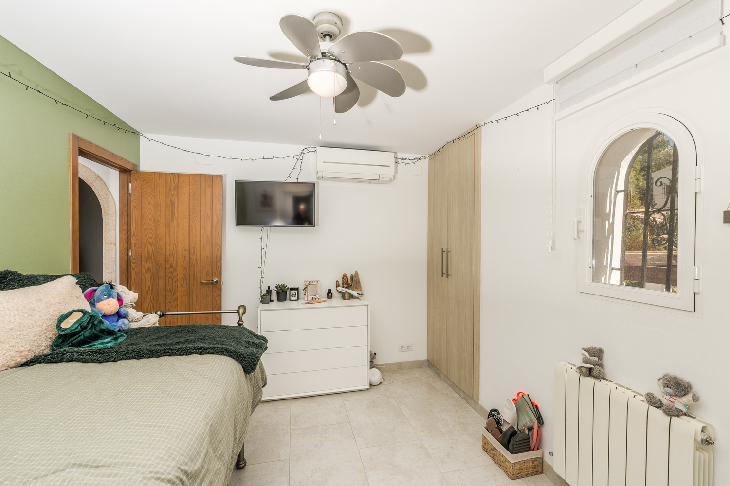 Lichte slaapkamer met een groene accentmuur, inbouwkasten en een boograam. Voorzien van een plafondventilator, airconditioning en centrale verwarming.