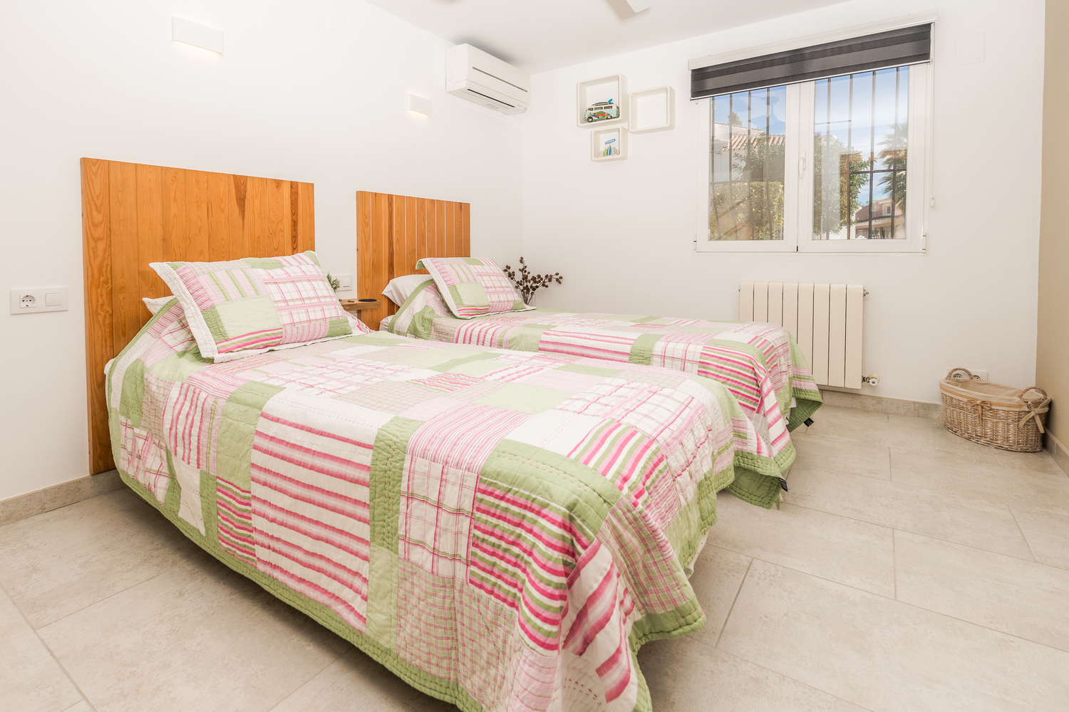 Slaapkamer met twee eenpersoonsbedden, houten hoofdborden en airconditioning. Voorzien van een lichte tegelvloer, radiator en raam met beveiligingsstangen.