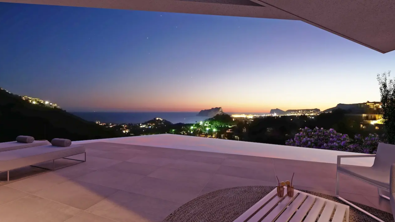 Terras met overloopzwembad en panoramisch uitzicht op de kust bij zonsondergang. Voorzien van grootformaat tegels, modern buitenmeubilair en zicht op de Peñón de Ifach.