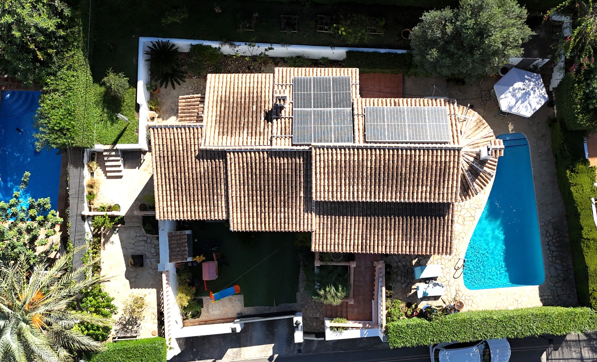 Bovenaanzicht van de villa met terracotta dakpannen en zonnepanelen, het privézwembad en een mediterrane tuin met een speelgedeelte voor kinderen.
