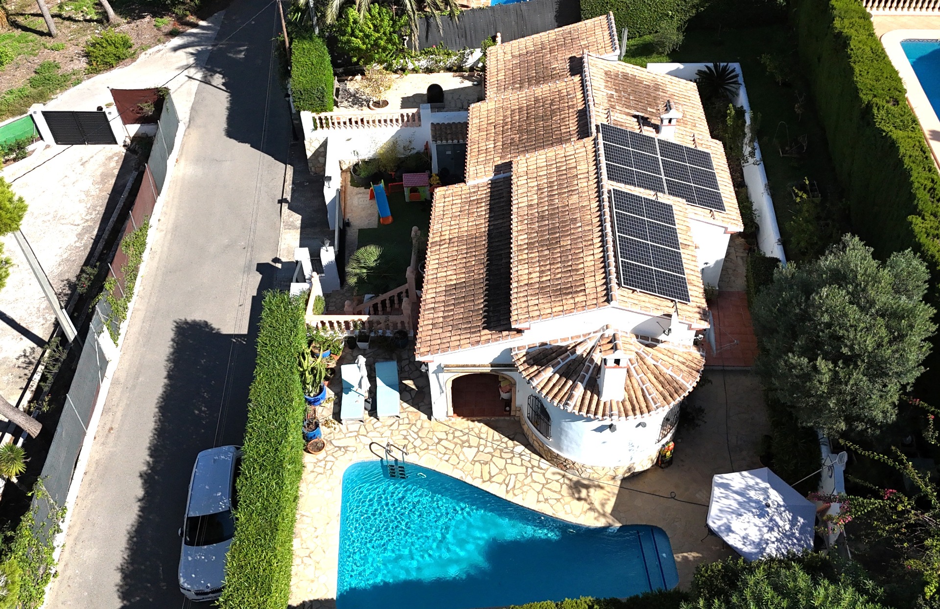 Luchtfoto van de villa met privézwembad, zonnepanelen op het pannendak en een kinderspeelplaats op het omheinde perceel.