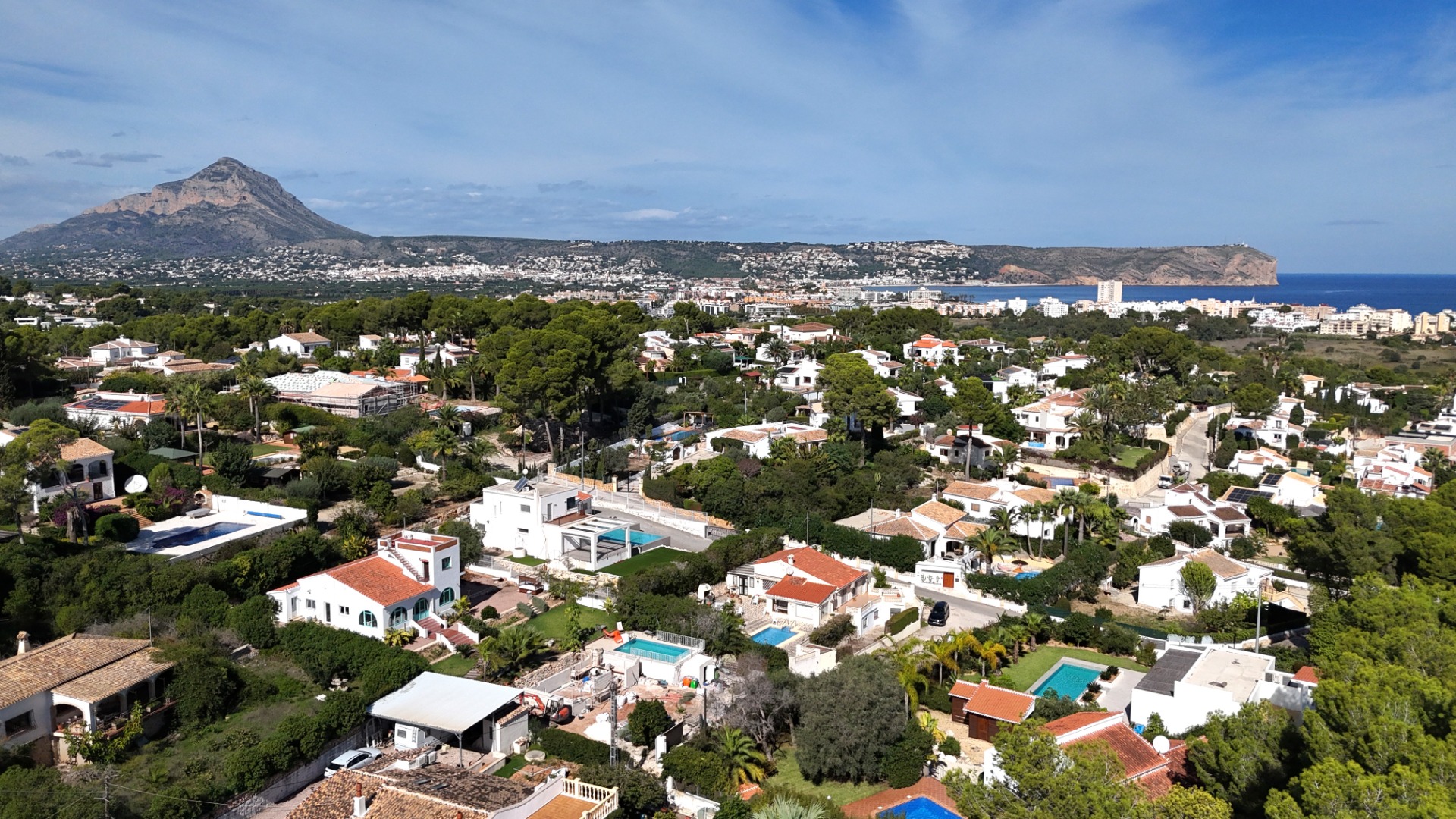 Panoramisch luchtfoto van de wijk Toscal in Jávea, met de Montgó-berg, Cabo San Antonio en de Middellandse Zeekust onder een heldere hemel.