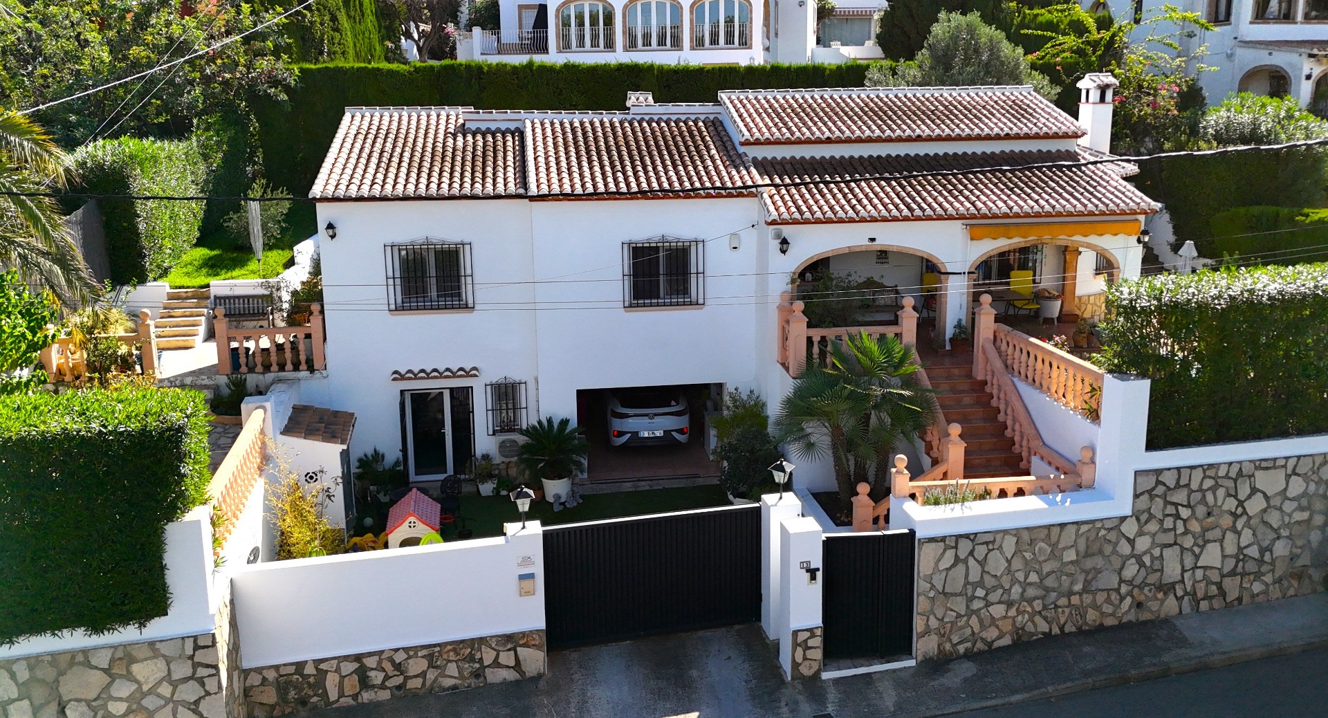 Vooraanzicht van een mediterrane villa met twee verdiepingen, witte gevel, terracotta dak, inpandige garage en een overdekt terras met stenen balustrades.