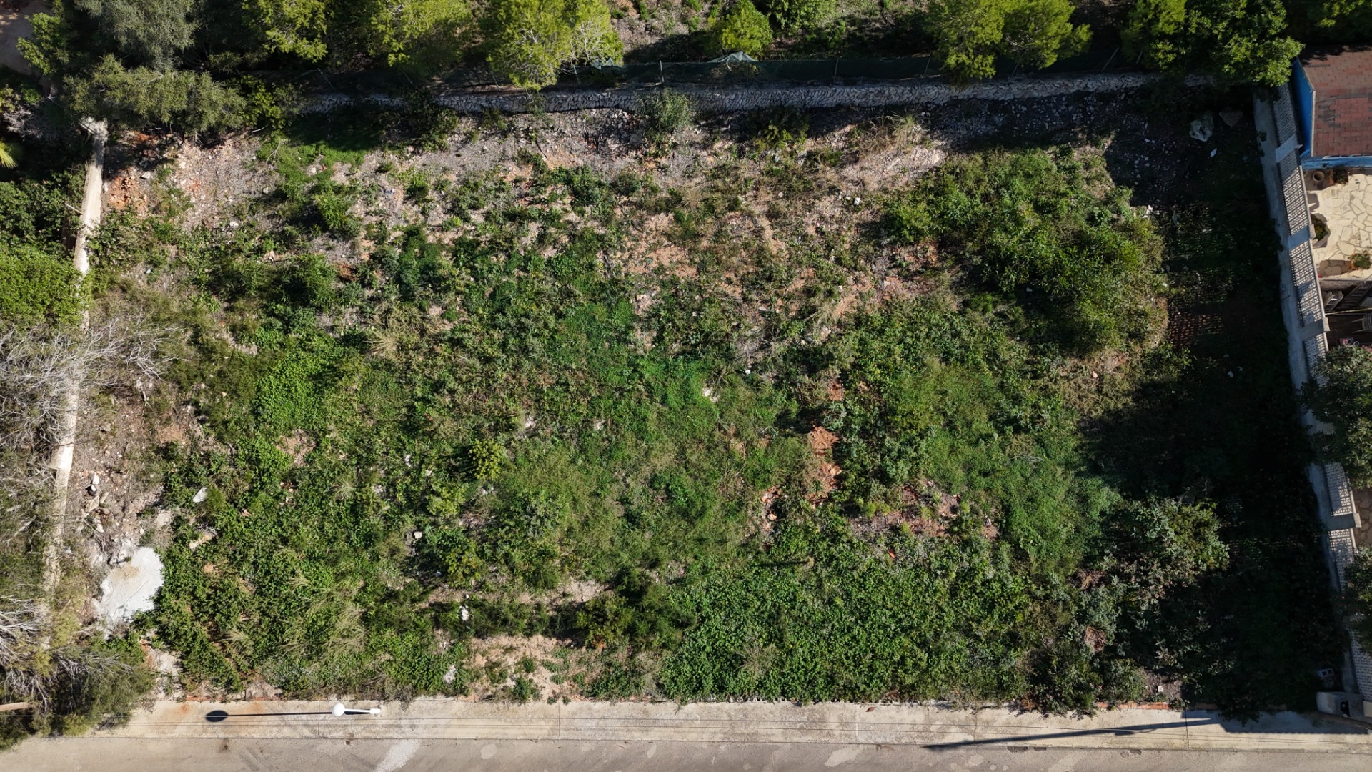 Luchtfoto van het vlakke perceel van 889 m² in Pinosol, met de rechthoekige indeling, natuurlijke begroeiing en directe toegang vanaf de verharde woonstraat.