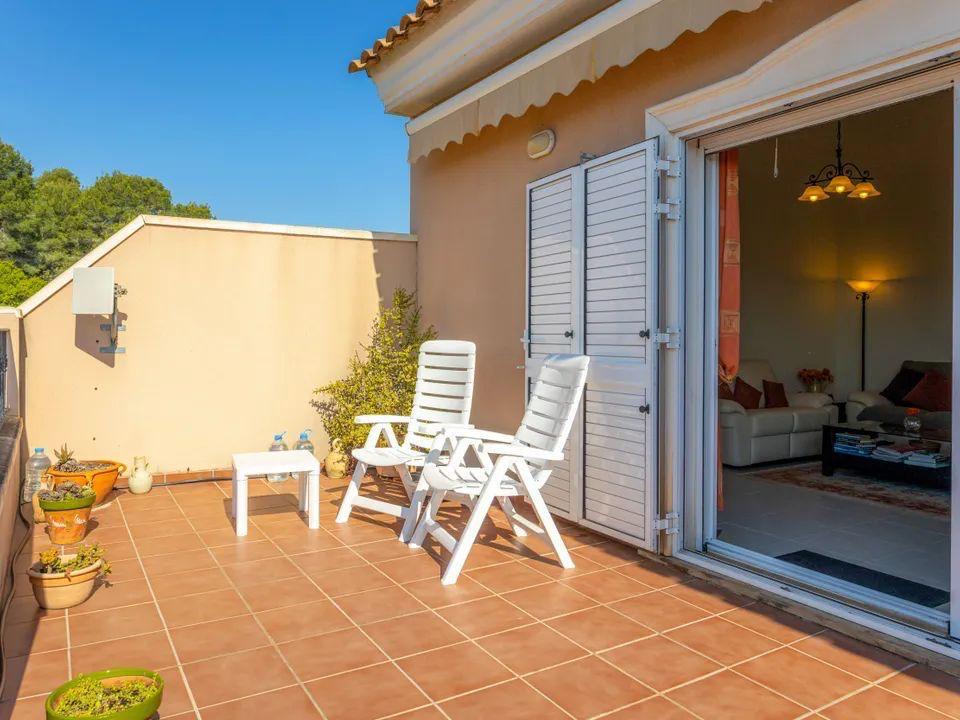 Buitenterras met terracotta tegels, witte klapstoelen en directe toegang tot de woonkamer via een schuifpui met witte mallorquina luiken.