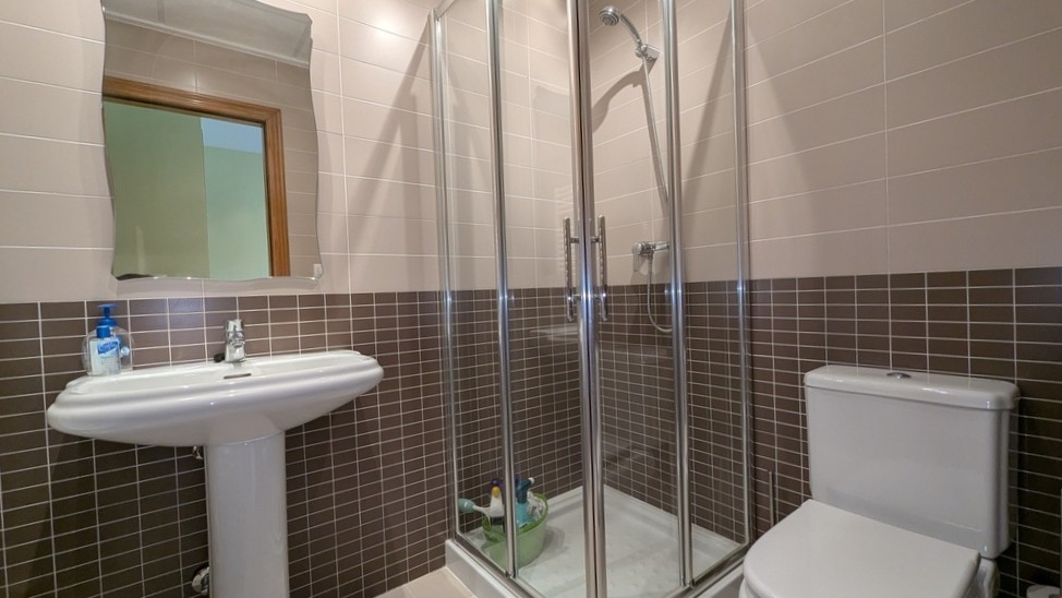 Functionele badkamer met een glazen hoekdouche, kolomwastafel en tweekleurige wandtegels in bruin en beige.