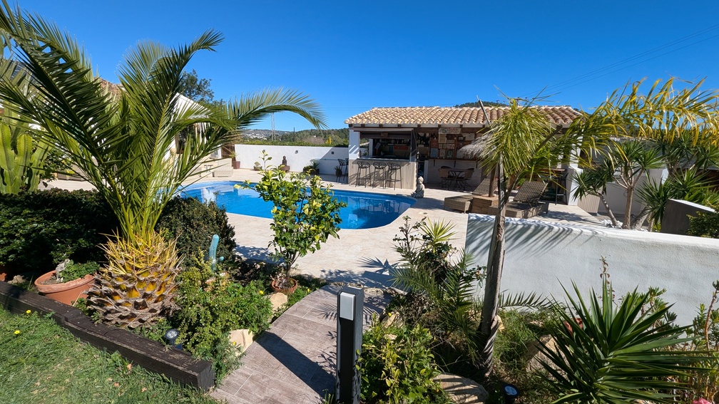 Buitenzwembad met stenen terras, mediterrane tuin met palmbomen en een volledig uitgeruste overdekte buitenkeuken met bar en krukken.
