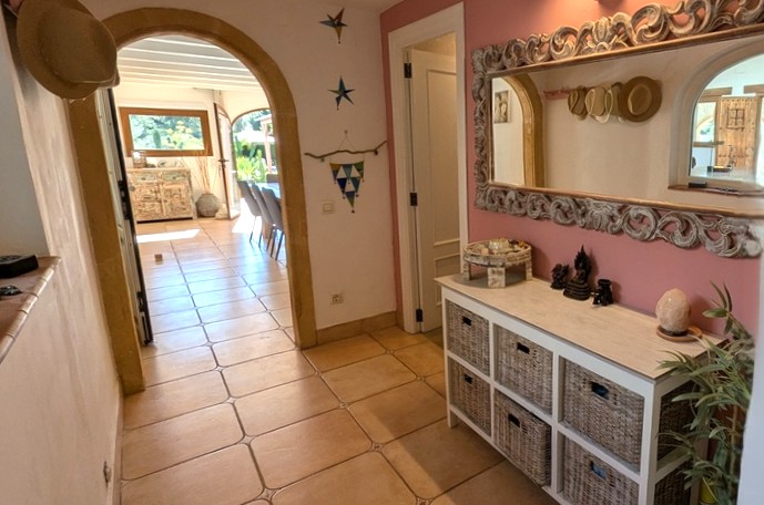 Entreehal met een traditionele Tosca stenen boog, terracotta tegelvloer en een sierlijke spiegel boven een dressoir met rieten manden.