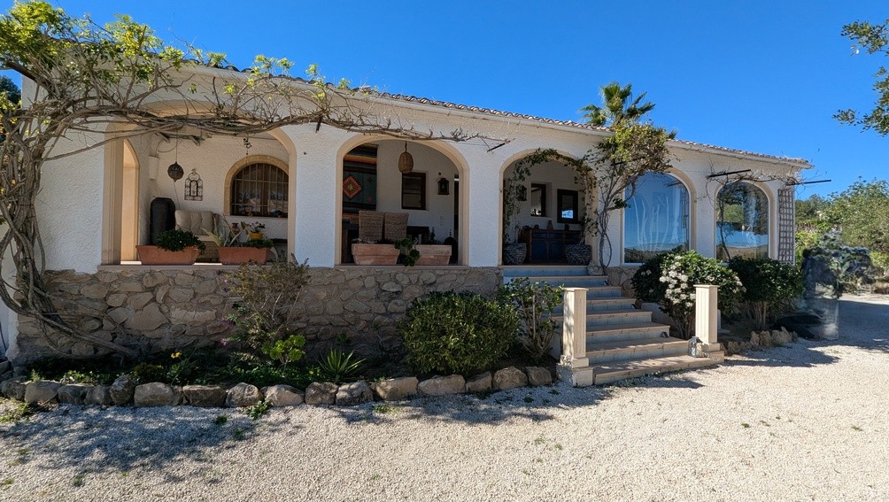 Gevel van de villa in finca-stijl met een traditionele naya met bogen, natuurstenen onderbouw en een toegangstrap met klimplanten.