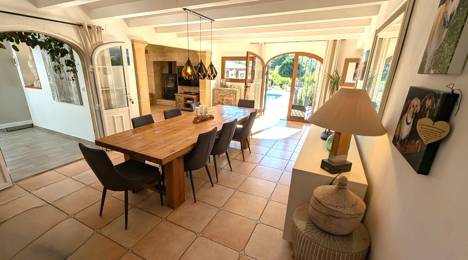 Lichte eetkamer met massief houten tafel, witte balkenplafonds en terracotta vloertegels. De glazen toogdeuren bieden directe toegang tot het terras en het zwembad.