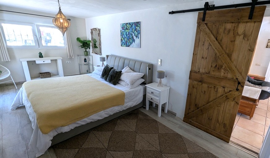 Lichte slaapkamer met een rustieke houten schuifdeur, gestoffeerd hoofdbord en een decoratieve Marokkaanse hanglamp op een vloer met houtlook.
