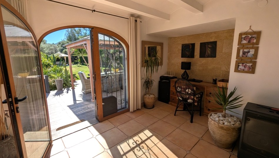 Lichte werkkamer met terracotta vloertegels, natuurstenen wand en houten boogdeuren die direct toegang geven tot het zonnige terras en de tuin.