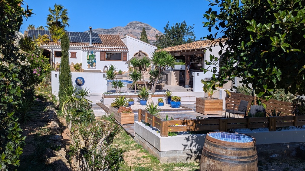 Mediterrane tuin met terrasvormige niveaus, buitenkeuken en villa met zonnepanelen, met direct uitzicht op de iconische Montgó-berg.