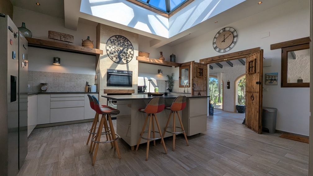 Moderne keuken met een glazen dakkoepel, centraal eiland met zitplaatsen en traditionele houten deuren die toegang bieden tot de naya.